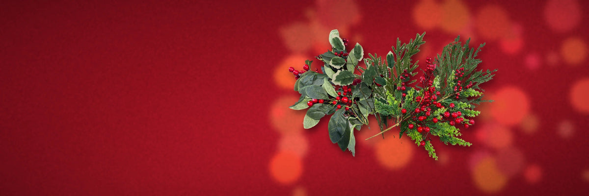 Red berry and leaf sprays with frosted pine picks on a deep red velvet background with soft bokeh.
